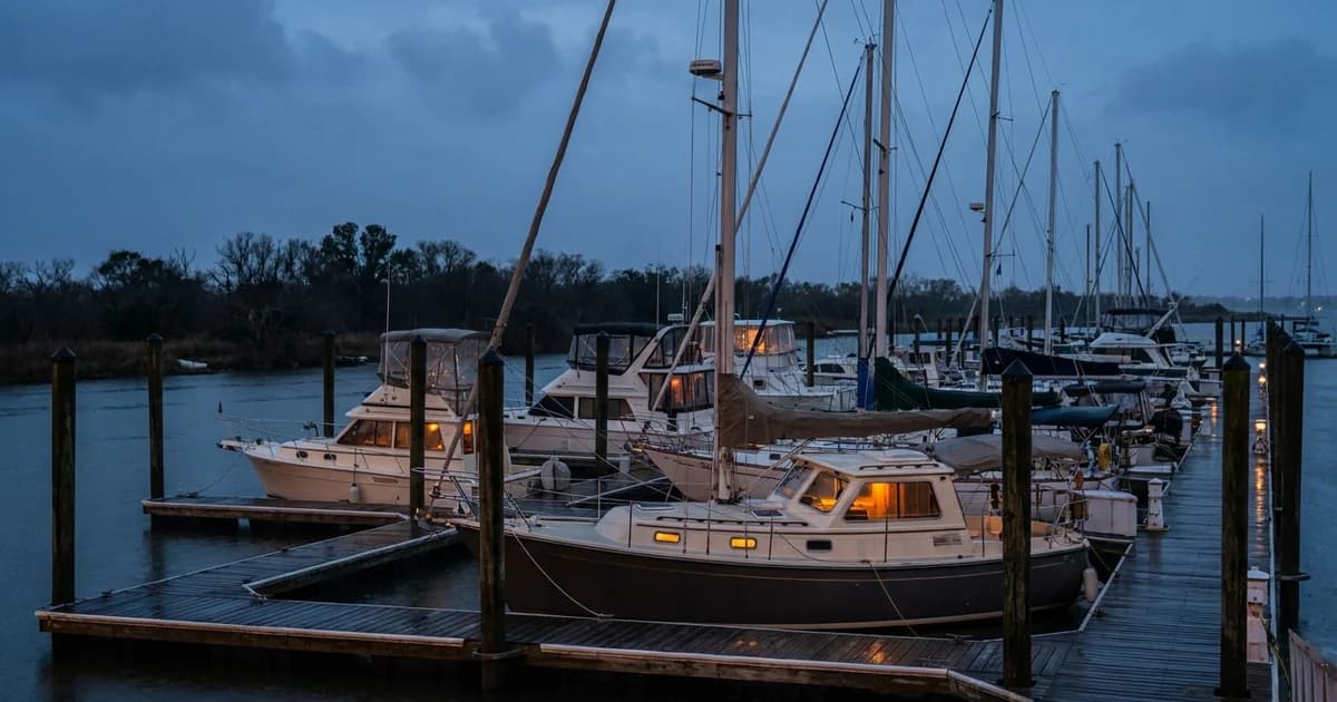 Galveston Bay area marina at dusk with rows of boats in floating slips and a dark, unlit shoreline behind the docks after a storm.